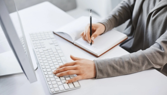 Woman typing on laptop and wrting on a notebook